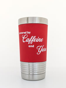 Image shows a stainless steel tumbler wrapped with a removable silicone sleeve that has been laser engraved with the phrase "Powered by Caffeine and Yarn" in white letters on a red background.  